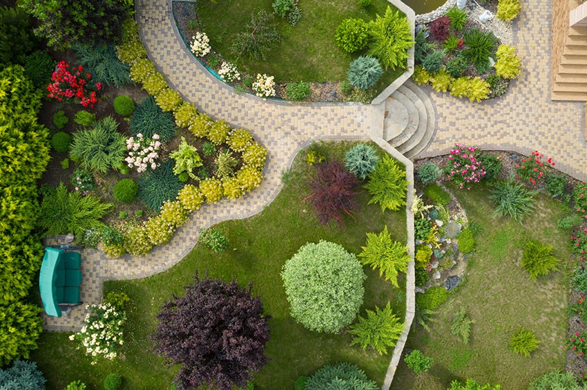 Photo taken from above by flying drone of a very well landscaped yard with walkways, trees, and shrubs